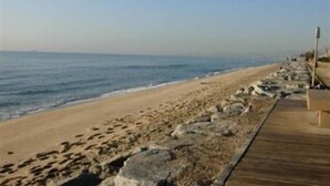 A beach with a wooden boardwalk and large rocks along the shore.