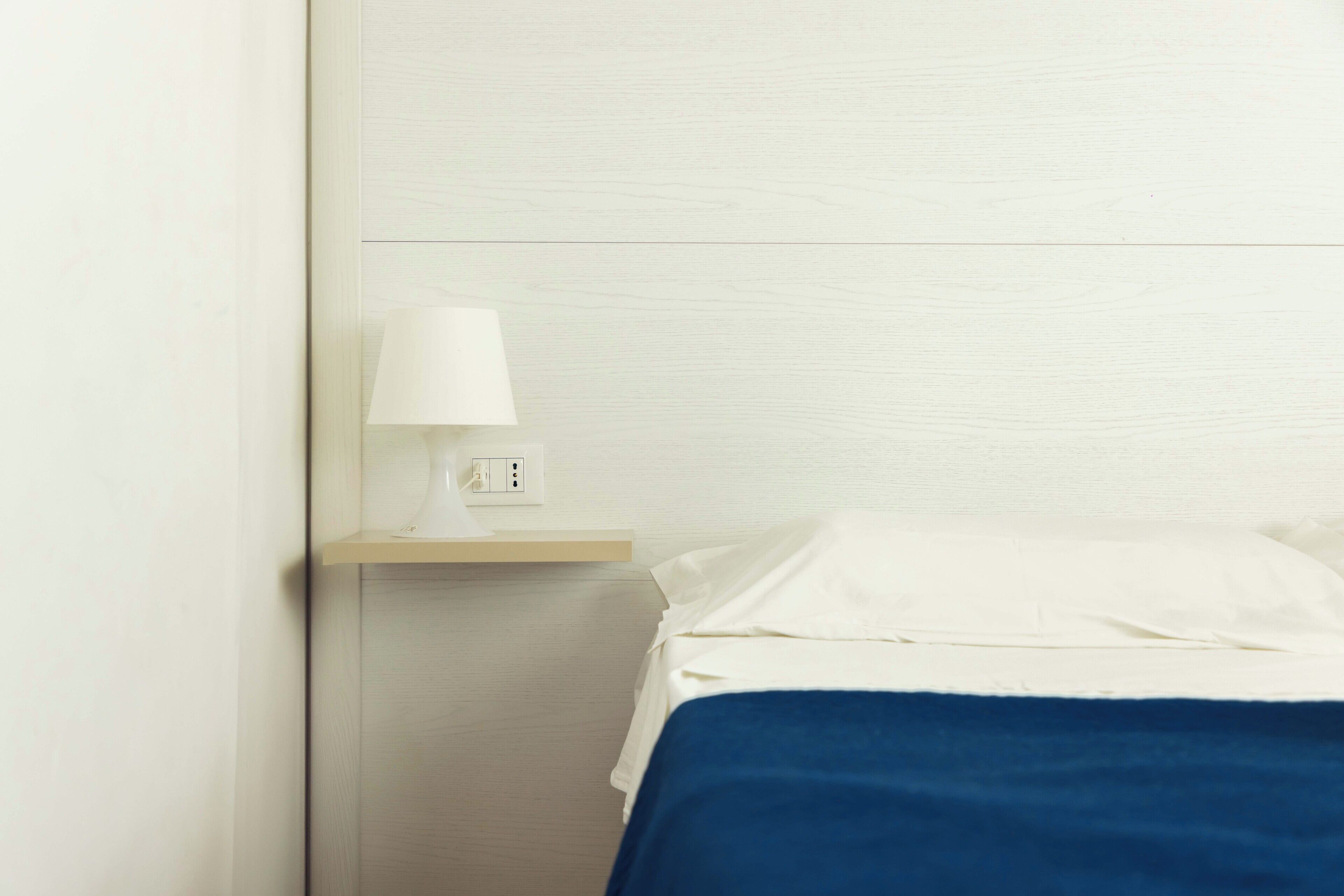 A hotel room with a bed, a nightstand, and a lamp.