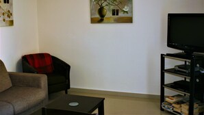 Ein Wohnzimmer mit einer Couch, einem Sessel, einem Couchtisch, einem Fernseher auf einem Schrank und einem Bild an der Wand.