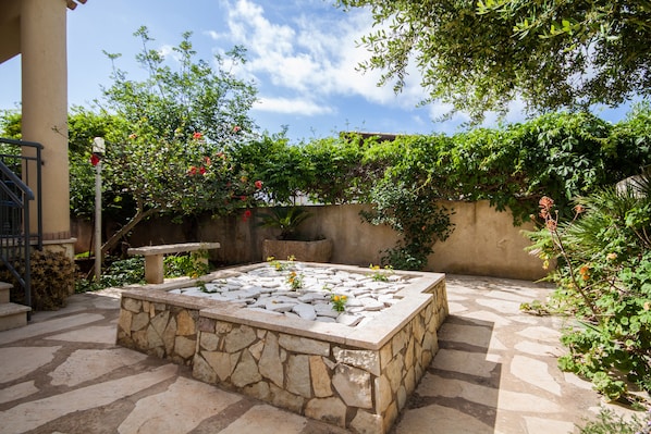 A stone-tiled courtyard with a central seating area, surrounded by lush greenery and flowering plants.