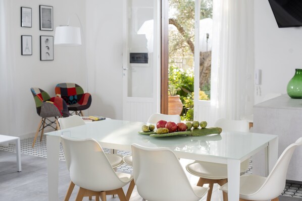 A modern dining area with a glass table, white chairs, and a variety of fruits.