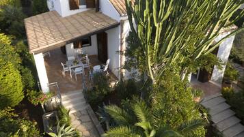 A white villa with a tiled roof, a patio with outdoor furniture, and a garden with various plants and a large cactus.