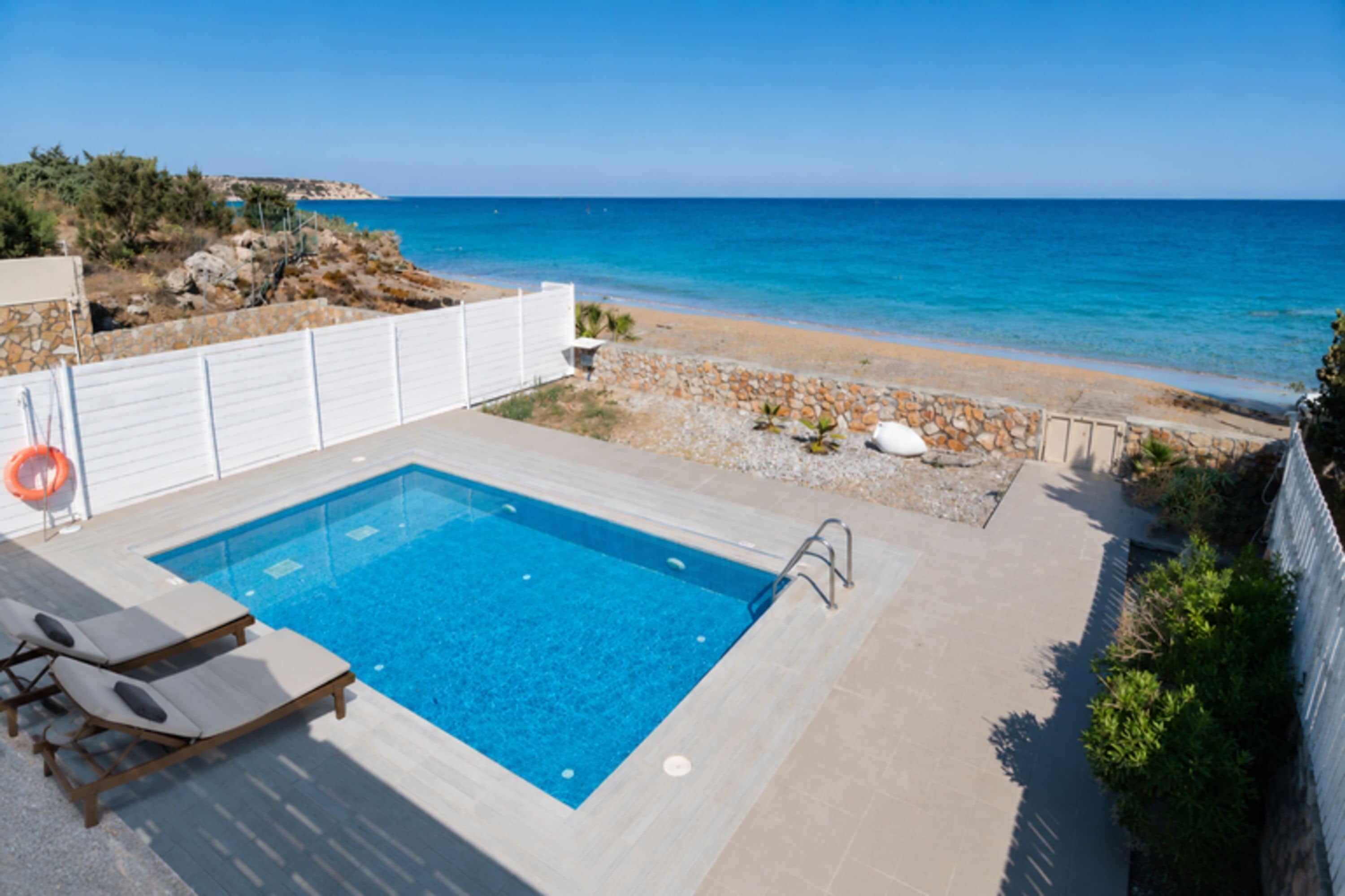 Ein Pool mit Blick auf das Meer, einem weißen Zaun und einen Strand.