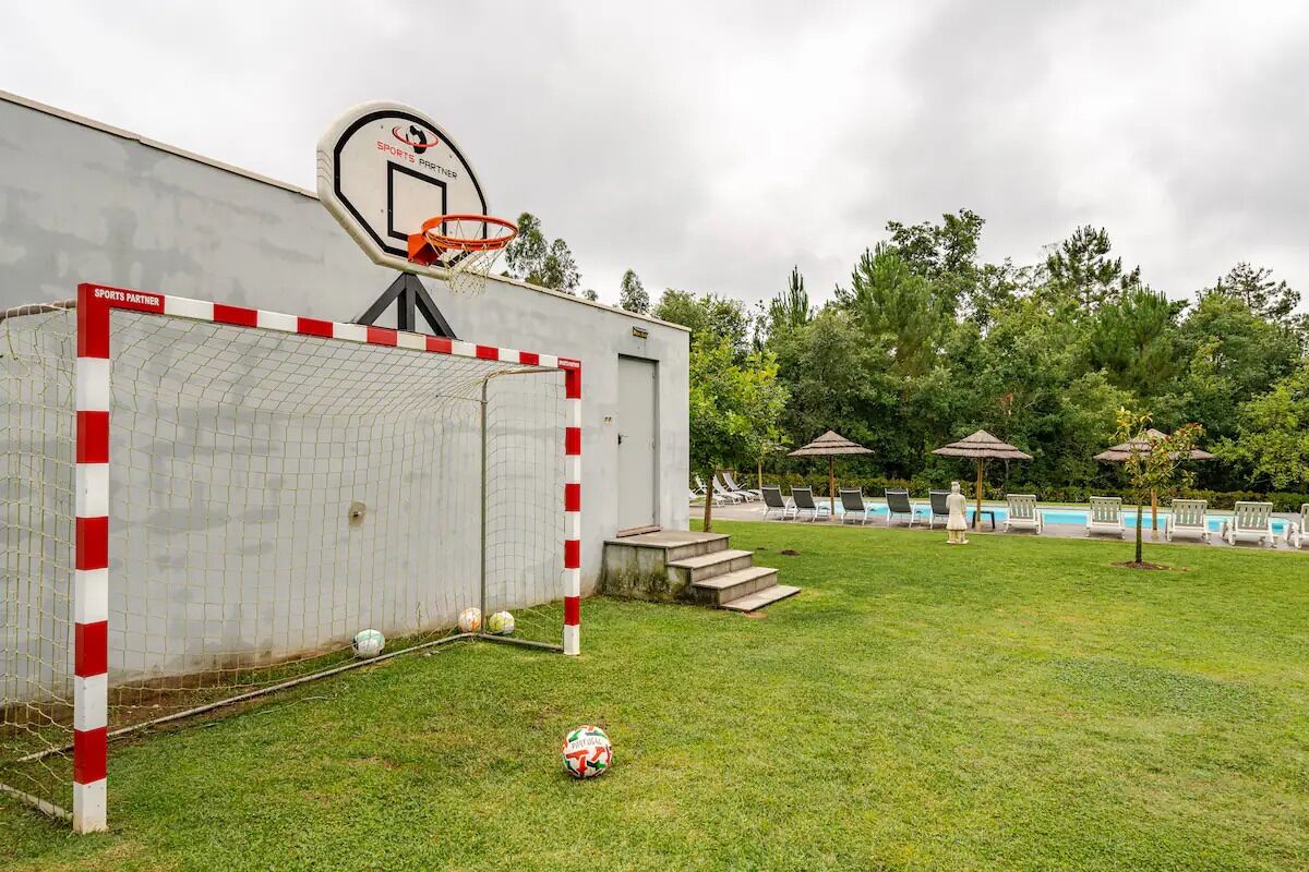 A sports facility with a basketball hoop, a soccer goal, and a swimming pool area with lounge chairs and umbrellas.
