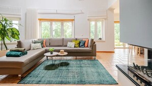 A modern living room with a sectional sofa, a flat-screen TV, and a large window providing natural light.