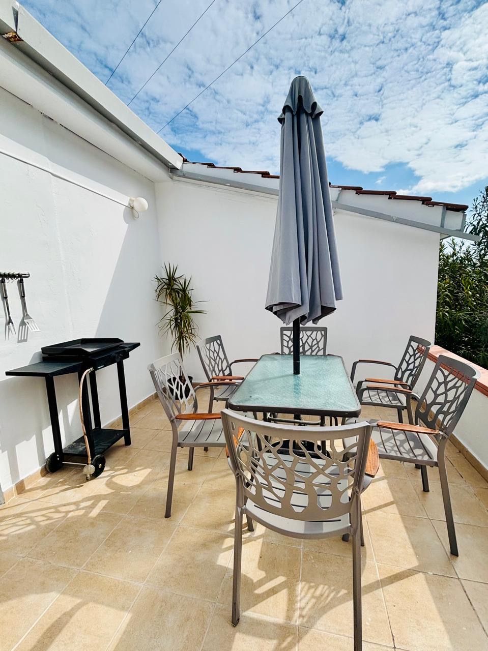 An outdoor patio with a table and chairs, a table lamp, a potted plant, and a black cart.