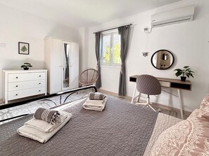 Een slaapkamer met een bed, bureau, stoel, kledingkast, spiegel en raam met gordijnen.