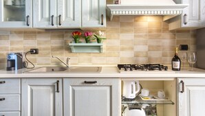 Una cocina con alacenas blancas, estufa a gas, cafetera y una botella de vino.