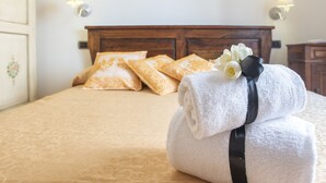 Una cama bien hecha con una colcha estampada, dos almohadas y una toalla blanca enrollada con una cinta negra y una flor.