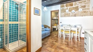 Habitación con cabina de ducha de vidrio, zona de comedor con mesa y sillas, sofá y pared de piedra con placas decorativas.