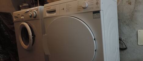 A front-loading washing machine with a control panel, a dryer, and a wall-mounted electrical outlet.