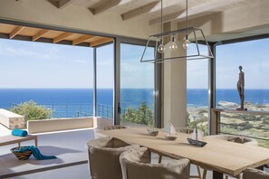 A modern dining area with a large table, chairs, and a view of the ocean.