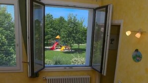 A room with a view of a playground, a table with a laptop, and a radiator.