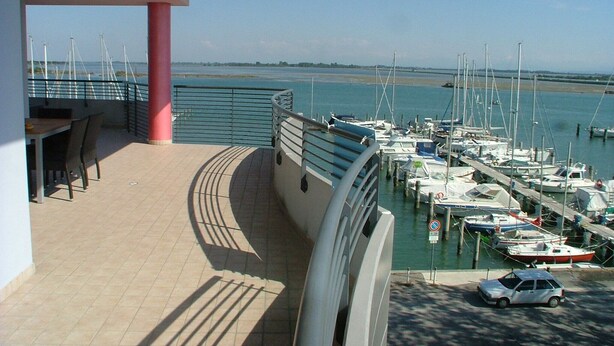 A balcony with a view of a marina, a dining area with chairs, and a car parked nearby.