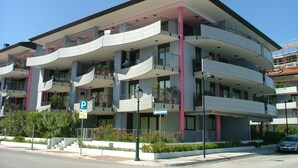 A multi-story residential building with balconies, a parking sign, and a pedestrian pathway.