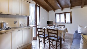 Eine Küche mit weißen Schränken, einem Esstisch für vier Personen und einem blauen Sofa in einem hellen Raum mit Holzbalken an der Decke.