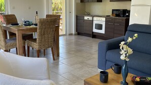 A modern kitchen with dark cabinets, a white refrigerator, and a dining area with wicker chairs and a table set for two. - VILLA VERDI D AIR CONDITIONED APARTMENT WITH TERRACE AND PRIVATE GARDEN POOL (Montauroux)