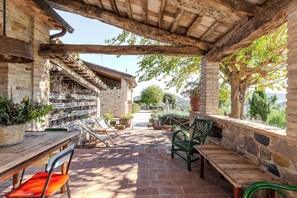 A covered patio with stone walls, wooden benches, and potted plants. - Deluxe Apartment The White Mulberry Tree Apartment (ARCEVIA)