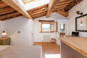 A room with a sloped ceiling, a bed, a desk with a laptop, a radiator, and a window with a view. - Deluxe Apartment The White Mulberry Tree Apartment (ARCEVIA)