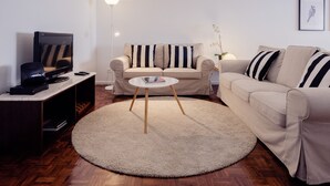 Uma sala de estar com sofá, mesa de centro, televisão e estante de livros.