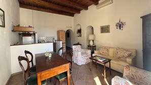 A cozy living room with a wooden dining table, a sofa, and a kitchen area with a refrigerator and a stove.