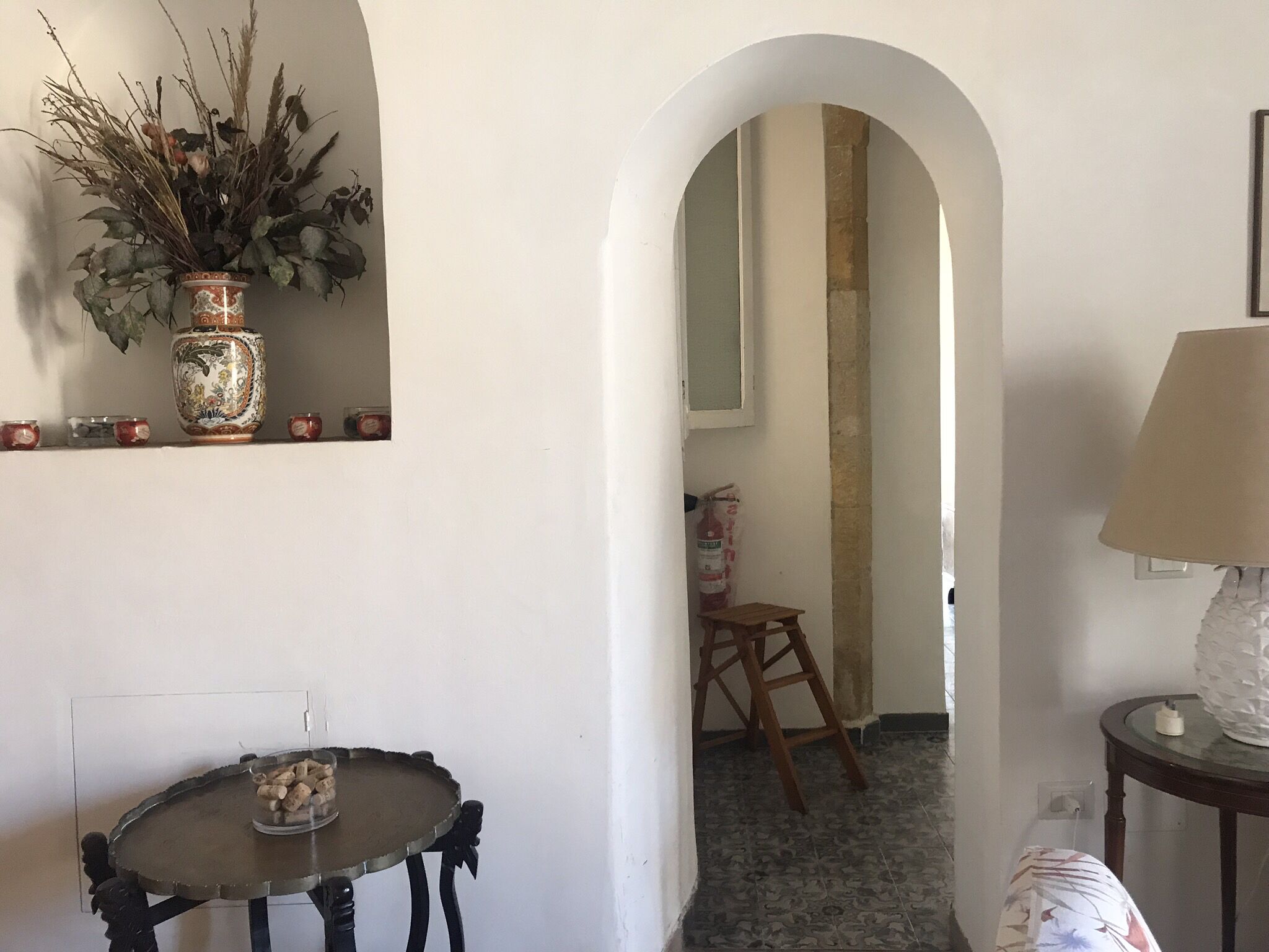 Una habitación con una mesa redonda, un taburete pequeño, un jarrón decorativo y un espejo.