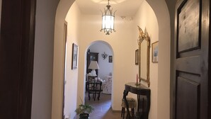 An arched hallway leading to a dining area with a chandelier, a table, chairs, and a potted plant.