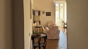 A hallway with a wooden ceiling, a lamp, a table with a basket and plant, and a chair with a floral pattern.