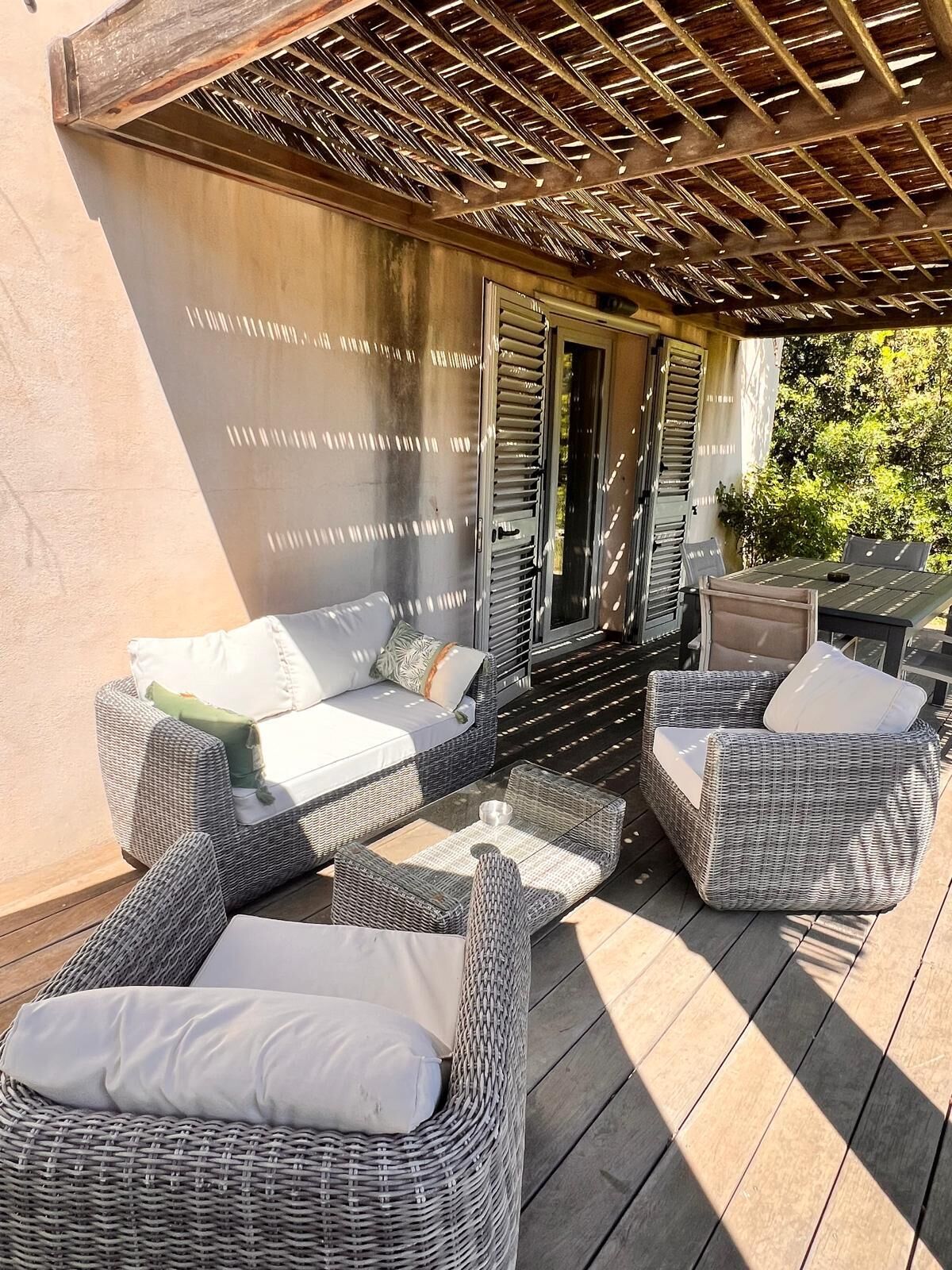 Een terras buiten met rieten meubels, waaronder banken en stoelen, en een pergola erboven.