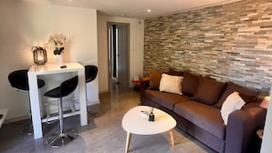 Ein modernes Wohnzimmer mit Steinwand, einem braunen Sofa, einem weißen Couchtisch und einem Essbereich mit zwei schwarzen Stühlen.