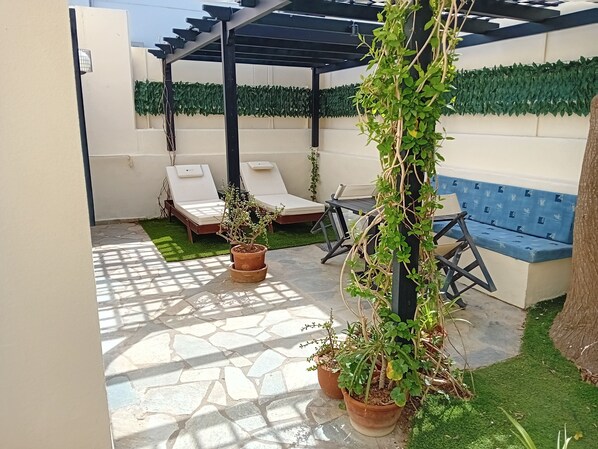 A patio with a pergola, two lounge chairs, a blue sofa, and potted plants.