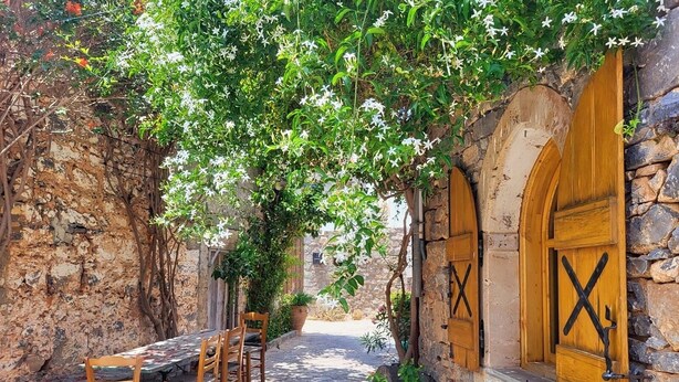 An outdoor seating area with stone walls, wooden tables, and chairs, surrounded by greenery and flowers. - Julie's studio in Kokkini Hani, 2 mins walk to beach. Near famous theme parks!  (Kokkini Hani)