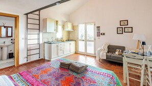 Quarto aconchegante com cama, tapete colorido, sofá, mesa de jantar e cozinha equipada com armários e pia.