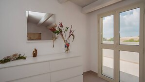 Una stanza con una cassettiera bianca, un vaso con fiori, una piccola scultura e un'ampia finestra vista spiaggia.