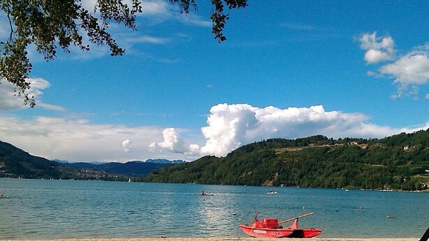 A lake with a red boat on the shore, surrounded by hills and clear skies.