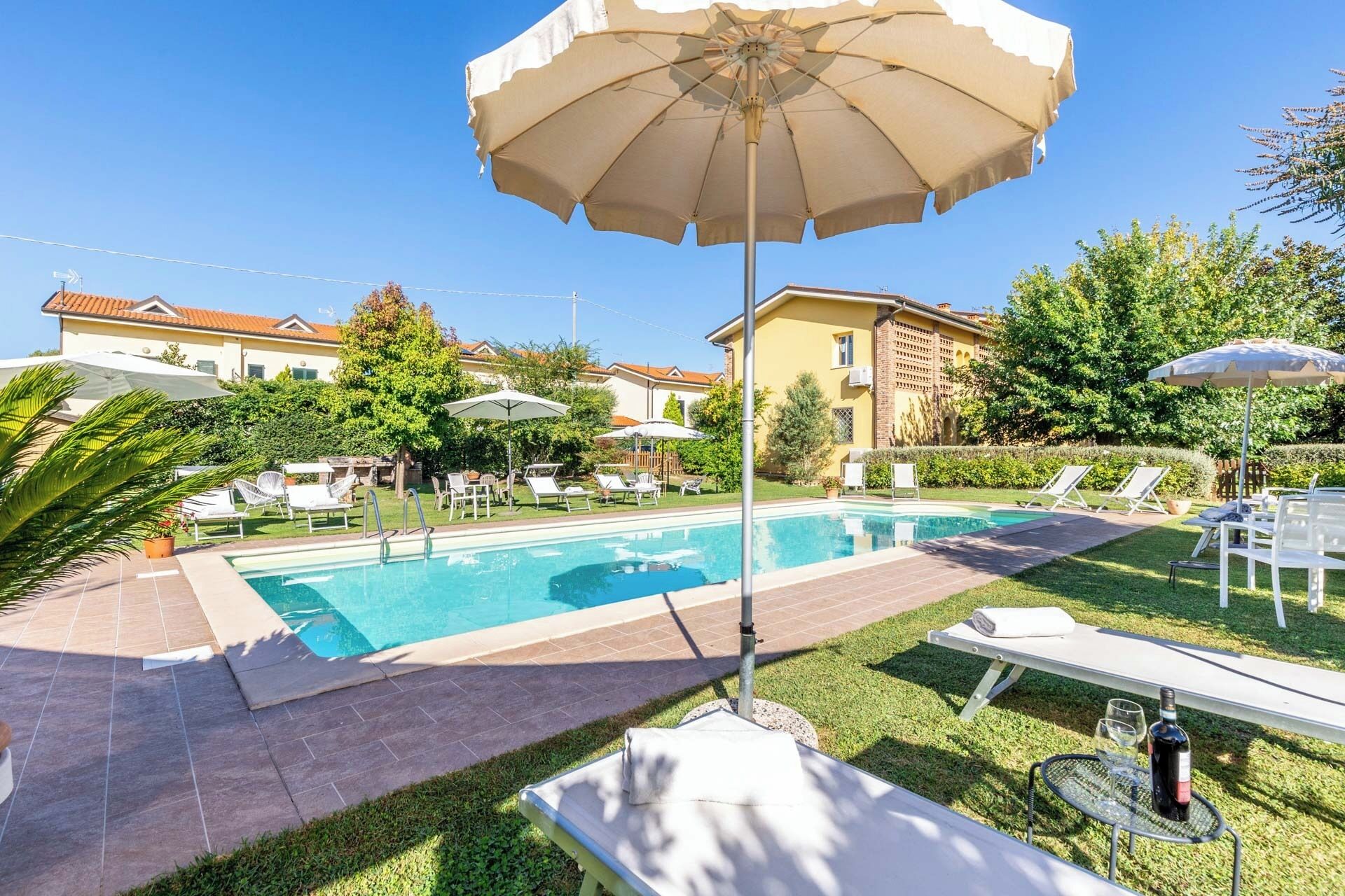 A swimming pool with lounge chairs and umbrellas, surrounded by well-maintained lawns and buildings.