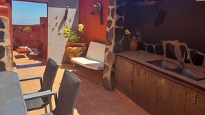 A patio with a dining area, a stone wall with a sink, and a red wall with decorative elements.