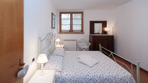 A bedroom with a bed, bedside table, lamp, chair, dresser, window, and radiator. - WINDMILL apartment with private terrace (Empoli)