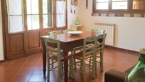 A dining area with a wooden table and chairs, a green vase, and a window with a view of trees. - WINDMILL apartment with private terrace (Empoli)