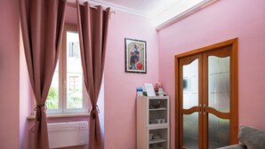 A room with pink walls, a radiator, a window with curtains, a cabinet with dishes, and a door with glass panels. - Wonderful beautiful apartment in the heart of Rome (Esquilino Colosseum area) (Roma)