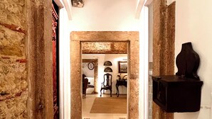 A hallway with stone walls, a tiled floor, and a mirror reflecting a room with furniture. - Spirit of 1512 - Exquisite taste in the heart of Alfama (Lisboa)