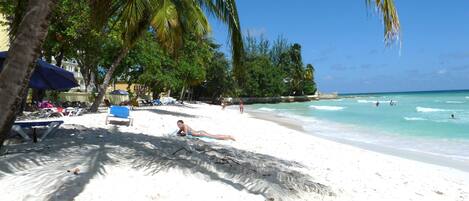 A beach with white sand, palm trees, and clear blue water.