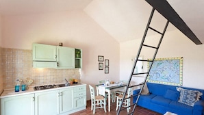 A compact kitchen with white cabinets, a tiled backsplash, and a dining area with a blue sofa and a ladder leaning against the wall.