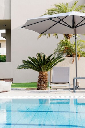 Ein Poolbereich mit Liege, Sonnenschirm und Palmen.