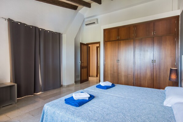 A hotel room with a large bed, a wardrobe, a bench, and a door leading to another room. - Villa with fantastic sea views. May 1600€/week (Porto Colom)