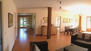 Amplia sala de estar con sofá, mesa de comedor y sillas. Cuenta con una zona de cocina con armarios y ventana.