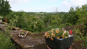 Un jardín con una maceta grande llena de flores, una maceta más pequeña con piedras y un rústico muro de piedra.