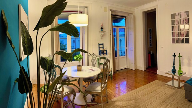 Un espace repas comprenant une table ronde et des chaises, un luminaire suspendu et de grandes plantes vertes.