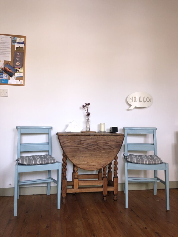 A wooden table with a vintage design, flanked by two light blue chairs with striped cushions. A bulletin board with various papers and a speech bubble decoration is mounted on the wall to the left. - Traditional Stone Village Apartment With Private Courtyard (Pentakomo)