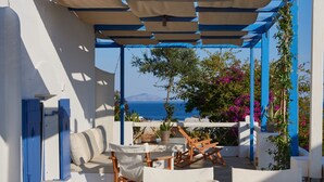 Un espace extérieur aménagé avec des tables et des chaises blanches, un plafond blanc et une vue sur la mer et les montagnes.